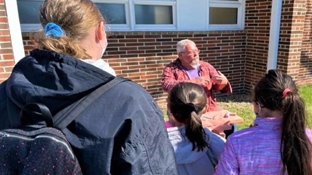 Man outdoors speaking in front of woman and 2 children